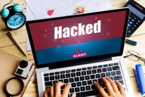 Hands typing on a laptop with a hacked alert on the screen